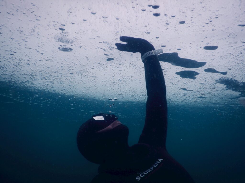 Anonymous diver in mask and wetsuit touching solid ice while swimming under seawater during freediving by Svetlana Obysova