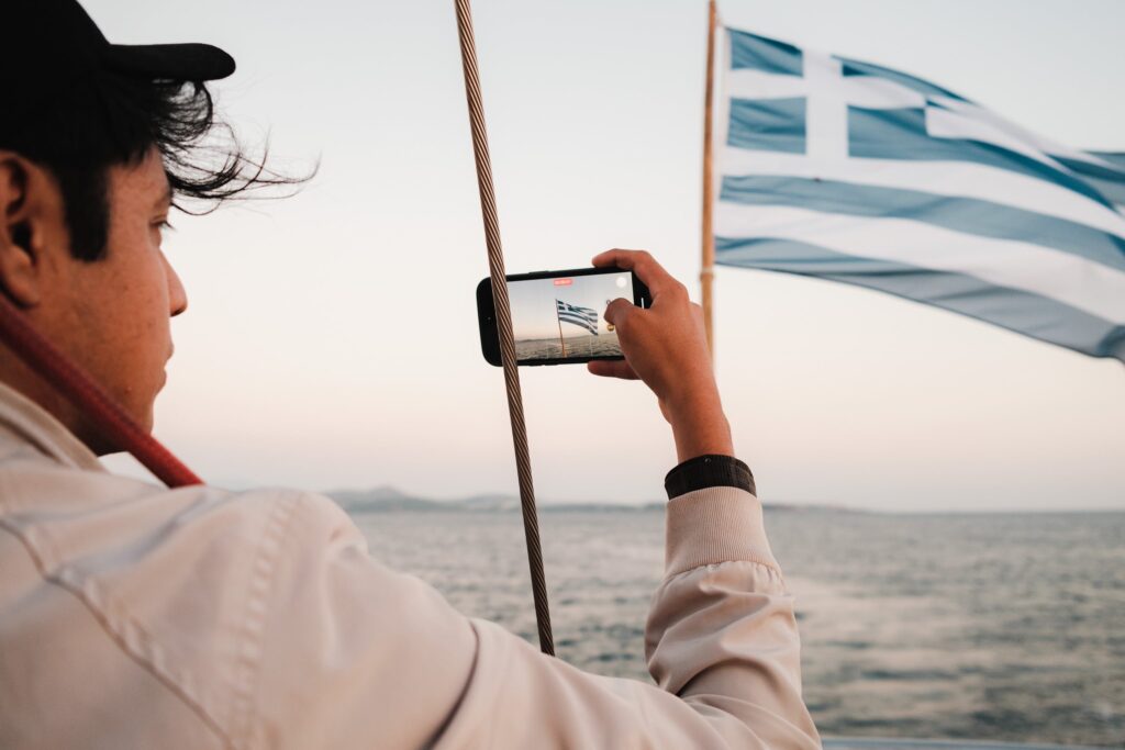 A man taking a photo of a greek flag on a boat by Airam Dato-on
