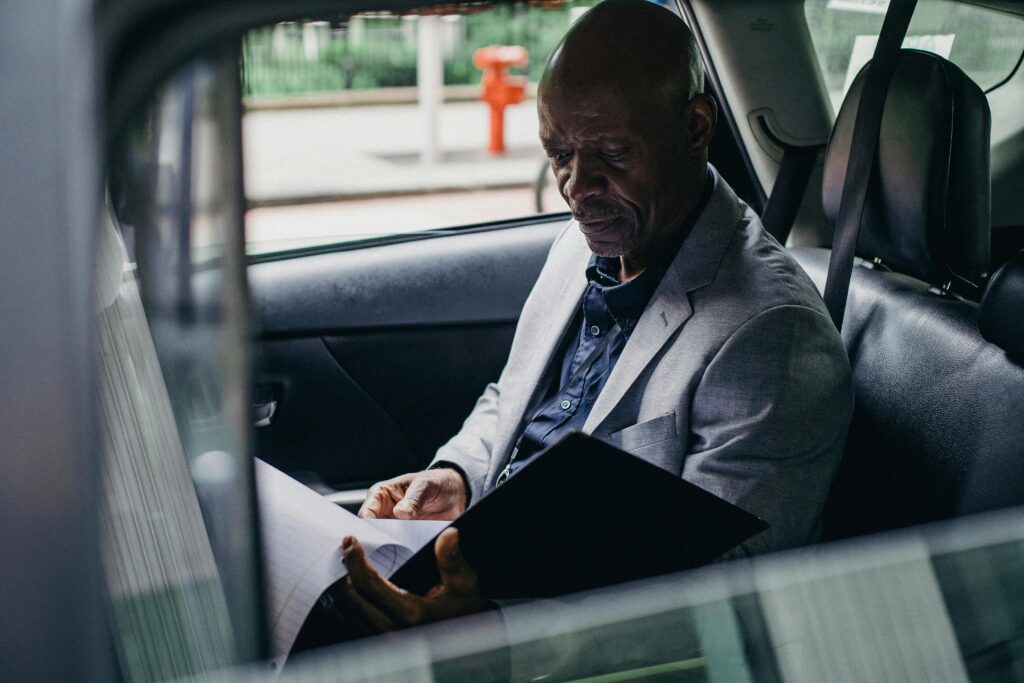 Side view serious African American businessman in formal clothes sitting in car back seat and reading documents by Ono  Kosuki