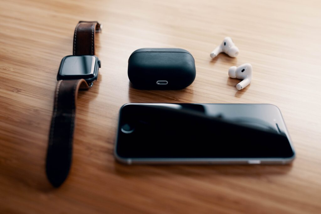 Black smart watch and TWS earbuds with charging case and smartphone lying on wooden table by Josh Sorenson