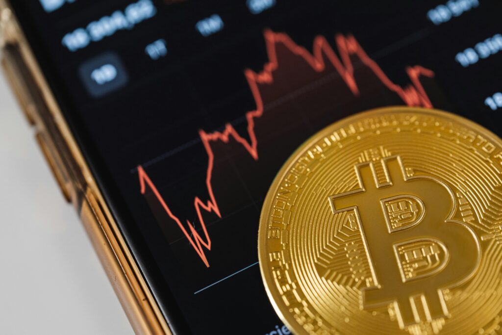 Close-up of a Bitcoin Coin Lying on a Screen Displaying a Stock Market Chart  by Karolina Grabowska